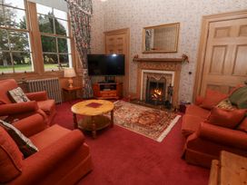 A sitting room with red armchairs a wooden coffee table a television and a fireplace at Cheviot Manor in Akeld near Wooler