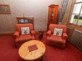 A sitting room with two red armchairs with deer cushions a wooden oval coffee table a small bookshelf a wooden cabinet a window with floral curtains and a radiator at Cheviot Manor in Akeld near Wooler
