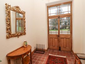 An entrance hall with wooden double doors a decorative mirror a small wooden table a vase a shoe rack and a rug at Cheviot Manor in Akeld near Wooler
