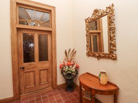 A hallway with a wooden door with textured glass panels a decorative mirror above a wooden console table with a vase and a floral arrangement in a black urn at Cheviot Manor in Akeld near Wooler