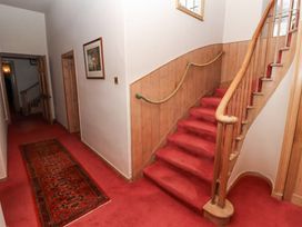A hallway with red carpeted stairs a red runner rug and wooden paneling at Cheviot Manor in Akeld near Wooler