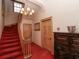 A hallway with a red carpeted staircase wooden doors a chandelier a mirror and a wooden cabinet at Cheviot Manor in Akeld near Wooler