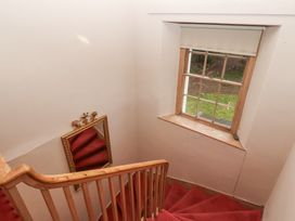 A staircase with red carpet and wooden railing with a window and framed mirror on the wall at Cheviot Manor in Akeld near Wooler