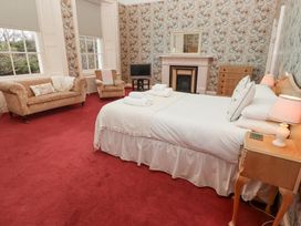 A bedroom with a double bed bedside tables with lamps armchair and sofa a television and fireplace at Cheviot Manor in Akeld near Wooler