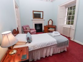 A bedroom with a single bed a bedside table lamp an armchair a fireplace a dressing table and a window at Cheviot Manor in Akeld near Wooler