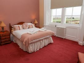 A bedroom with a double bed and bedside tables with lamps near windows showing a green landscape at Cheviot Manor in Akeld near Wooler