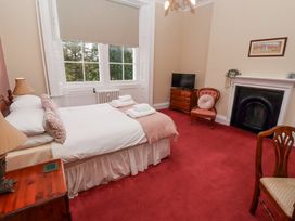 A bedroom with a double bed side tables lamps a dresser television a chair a fireplace and windows at Cheviot Manor in Akeld near Wooler