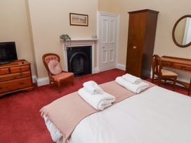 A bedroom with a bed, towels, a wooden chest of drawers, an armchair, a fireplace, a wardrobe, a dressing table with a chair and a mirror at Cheviot Manor in Akeld near Wooler