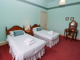 A bedroom with two single beds and wooden headboards a nightstand with a lamp and a vanity desk with a chair at Cheviot Manor Akeld near Wooler