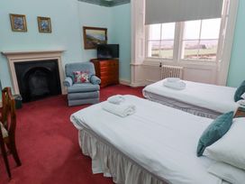 A bedroom with two single beds a blue armchair a wooden dresser and a fireplace at Cheviot Manor in Akeld near Wooler