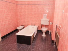A bathroom with a bathtub bidet toilet and radiator with pink tiled walls and dark tiled floor at Cheviot Manor in Akeld near Wooler