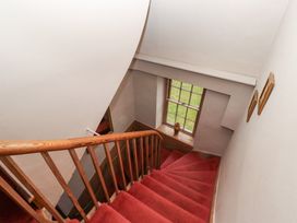A staircase with red carpet and wooden handrails next to a window with a vase at Cheviot Manor in Akeld near Wooler