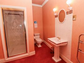 A bathroom with a shower enclosure toilet pedestal sink round mirror and wall lights at Cheviot Manor in Akeld near Wooler