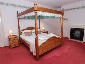 A bedroom with a wooden four-poster bed two bedside tables with lamps a fireplace and red carpet at Cheviot Manor in Akeld near Wooler