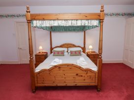 A bedroom with a wooden four-poster bed with side tables and lamps on a red carpet at Cheviot Manor Akeld near Wooler