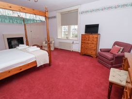 A bedroom with a four poster bed a wooden dresser with a television two armchairs and a window at Cheviot Manor in Akeld near Wooler