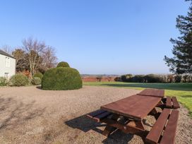 A picnic table on gravel in a garden with trimmed bushes and a house in the background at Cheviot Manor Akeld near Wooler
