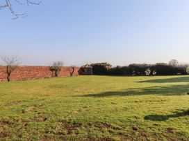 A grassy garden with a red brick wall and small trees at Cheviot Manor in Akeld near Wooler