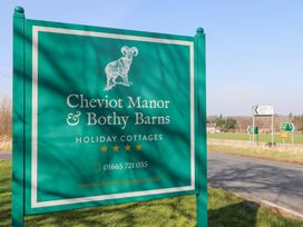 A green roadside sign for Cheviot Manor and Bothy Barns holiday cottages near a road with directional signs at Cheviot Manor in Akeld near Wooler