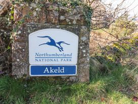 A stone sign for Northumberland National Park with Akeld below in a grassy area with branches and moss