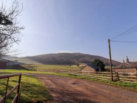 A rural landscape with a dirt road, fenced fields, buildings, and a hill in the background at Cheviot Manor in Akeld near Wooler
