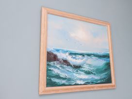 A framed painting of ocean waves crashing on rocks with birds flying in the sky at Sunny Side in Runswick Bay