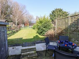 A garden with lawn and trees next to a patio with a table set with dark blue dishes and black chairs at Sunny Side in Runswick Bay