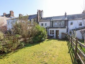A backyard with a grass lawn shrubs and small patio furniture behind terraced houses at Sunny Side in Runswick Bay