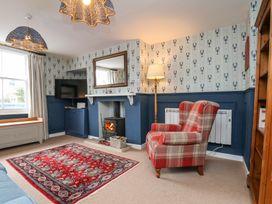 A living room with a red patterned rug a plaid armchair a fireplace television and blue and white wallpaper at Sunny Side in Runswick Bay