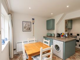 A kitchen with a wooden dining table and white chairs next to a window and a counter with appliances at Sunny Side in Runswick Bay