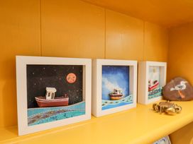 Three framed artworks of boats on water on a yellow shelf with a painted rock of a seagull and a brass crab figurine