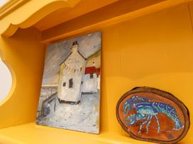 A painting of a white building with flags and a blue lobster painted on a wooden plaque on a yellow shelf at Sunny Side in Runswick Bay