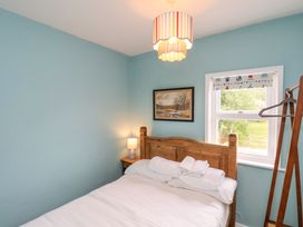 A bedroom with a wooden bed a nightstand with a lamp a window with a patterned blind and a wooden coat rack at Sunny Side in Runswick Bay
