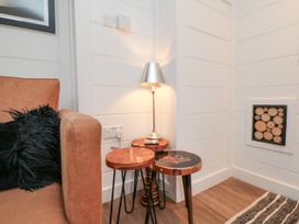 A corner with a brown sofa with a black pillow metal lamp and three small wooden tables with a wood log decoration in the wall at The Blacksmith's Shop in Staithes
