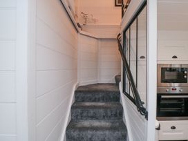 A carpeted staircase with white paneled walls and a black handrail next to a kitchen with built in oven and microwave at The Blacksmith's Shop in Staithes