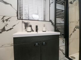 A bathroom sink with black cabinet a black faucet soap dispenser and a small mirror on a marble wall at The Blacksmith's Shop in Staithes