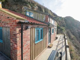 An exterior view of a house with brick and wooden walls blue window frames and a tiled roof on a hillside with a path and railing at The Blacksmith's Shop in Staithes