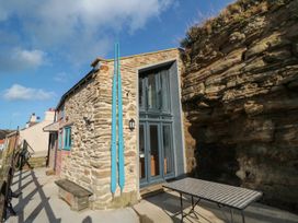An outdoor area with stone and brick walls featuring blue door and windows and a metal table by a rocky cliff at The Blacksmith's Shop in Staithes