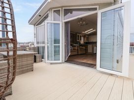 An outdoor patio with wicker furniture and a hanging chair next to an open door leading to a living area at Hazel Park Lodge HP4 in Rhyl