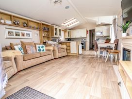 An open plan living area with a beige sofa and armchair a dining table with chairs a kitchen with cabinets and appliances and wooden flooring at Hazel Park Lodge HP4 Rhyl
