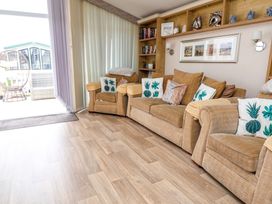 A living room with beige sofas and armchairs with patterned cushions and shelves with decorations at Hazel Park Lodge HP4 in Rhyl