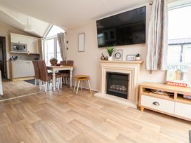 A living room with a fireplace dining table chairs and a kitchen in the background at Hazel Park Lodge HP4 in Rhyl