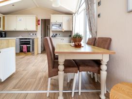 A dining area with a wooden table and four brown chairs next to a kitchen with white cabinets at Hazel Park Lodge HP4 in Rhyl