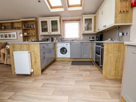 A kitchen with wood and gray cabinets a washing machine oven kettle and window blinds at Hazel Park Lodge HP4 in Rhyl