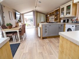 A kitchen and dining area with a wooden table and chairs a washing machine and a TV mounted on the wall at Hazel Park Lodge HP4 in Rhyl
