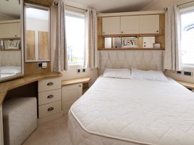 A bedroom with a bed two pillows curtains a corner desk with drawers and a mirror and cabinet above the bed at Hazel Park Lodge HP4 in Rhyl
