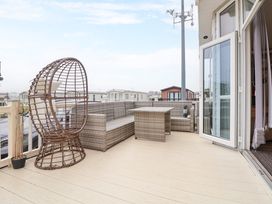 An outdoor deck area with wicker seating and a table next to an open patio door at Hazel Park Lodge HP4 in Rhyl