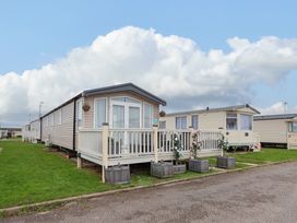 A row of beige mobile homes with porches and flower pots on a grassy area at Hazel Park 11 HP11 in Rhyl