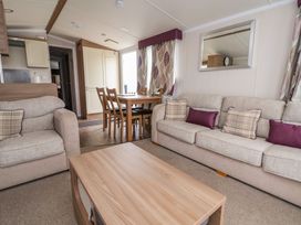 A living room with beige sofas, a wooden coffee table, dining table with chairs near a window and patterned curtains at Hazel Park 11 HP11 in Rhyl