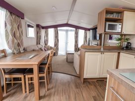 A dining area with wooden table and chairs connected to a living room with sofas and curtains at Hazel Park 11 HP11 in Rhyl